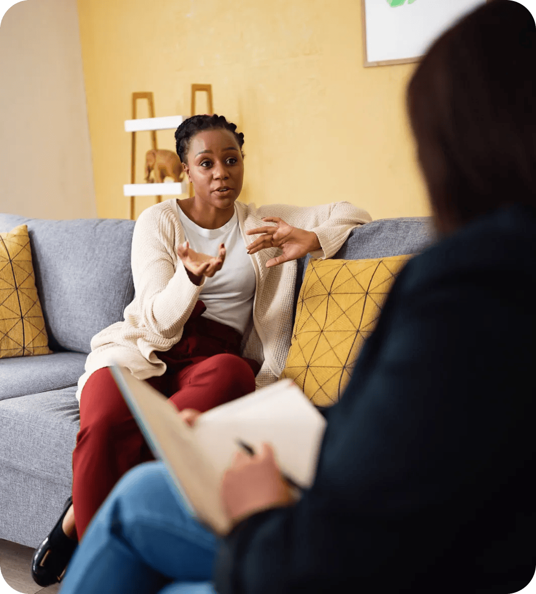 Two people having a conversation in a living room, with one person gesturing while speaking and the other taking notes.